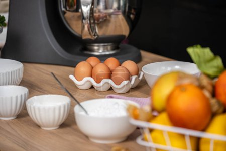 organized kitchen counter displays ingredients for baking, featuring a carton of eggs, bowls of flour and sugar, and fresh fruits, setting the scene for a home cooking adventure. High quality photo