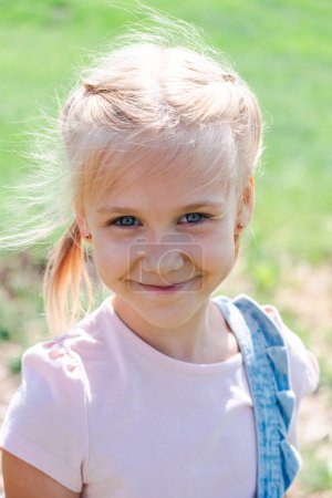 Ein fröhliches junges Mädchen lächelt im Freien und verkörpert in ihrer sonnigen, grasbewachsenen Kulisse kindliches Glück, gesundes Leben und die Vitalität der Natur. Hochwertiges Foto