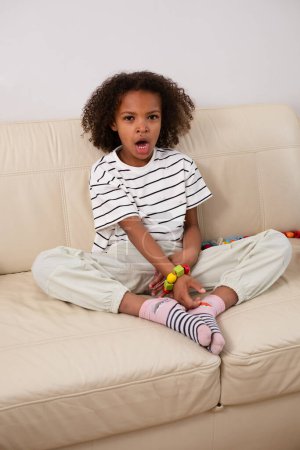 Seated comfortably, a yawning and tired mixed race girl is working on a bead craft, dressed in striped shirt, showing a focused engagement. Suitable for educational and toy therapy. High quality photo