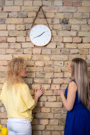 Dos socios de negocios, la mujer de pie bajo un reloj y hablar, lo que sugiere un momento de urgencia y la importancia de la puntualidad en el crecimiento profesional. Foto de alta calidad