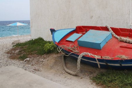 Foto de Barco de pesca tradicional rojo y azul y sombrilla blanca azul en la playa en el pueblo de Kokkkari en la isla griega de Samos - Imagen libre de derechos