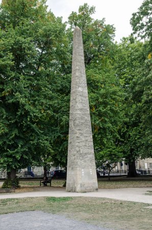 Photo for View of the historic stone obelisk erected by Beau Nash in honour of Frederick, Prince of Wales in 1738 in Queen Square, Bath, Somerset.  Cloudy summer afternoon. - Royalty Free Image