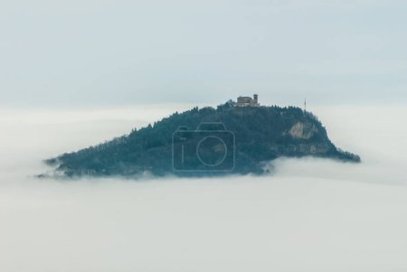 Téléchargez les photos : Colline et église submergées par le brouillard - en image libre de droit