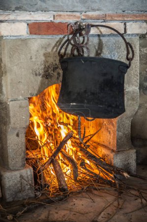 Téléchargez les photos : Old blackened pot hanging on the chimney and fire - en image libre de droit