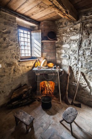 Téléchargez les photos : Cheminée allumée et ustensiles dans la maison de l'agriculteur avec cheminée - en image libre de droit