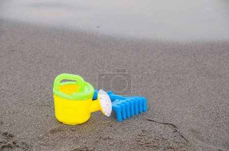 Téléchargez les photos : Arrosoir jouet et râteau sur le bord de la mer - en image libre de droit