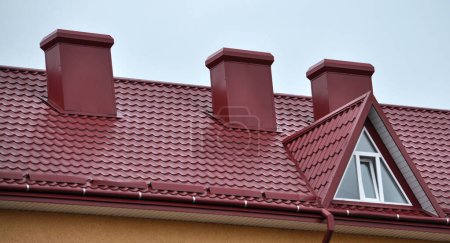 Foto de Una chimenea en el techo de una casa cubierta con azulejos metálicos o un perfil metálico - Imagen libre de derechos