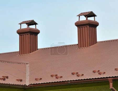 Téléchargez les photos : Une cheminée sur le toit d'une maison recouverte de tuiles métalliques ou d'un profil métallique - en image libre de droit