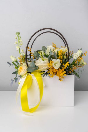 Photo for Beautiful bouquet of flowers and greenery in a white bag with yellow ribbon - Royalty Free Image