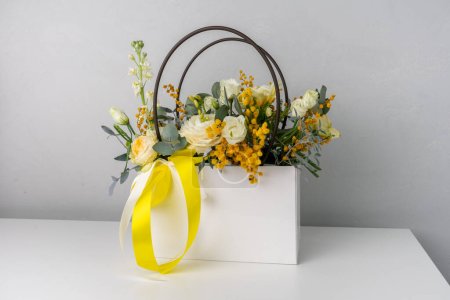 beautiful bouquet of flowers and greenery in a white bag with yellow ribbon