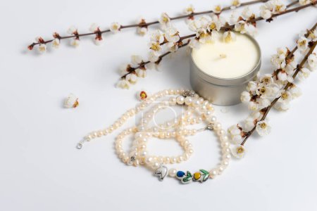 Eine Perlenkette, eine Kerze und blühende Zweige auf weißem Hintergrund