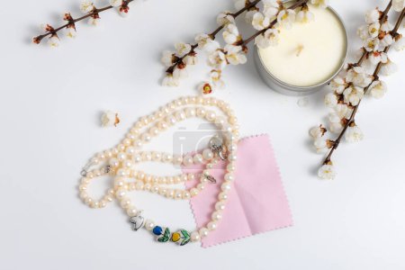 Photo for A string of pearls, a candle and blooming branches on white background - Royalty Free Image