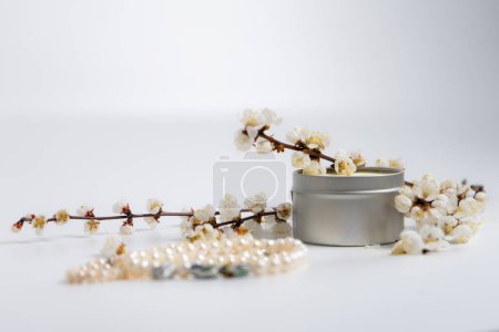 Une chaîne de perles, une bougie et des branches en fleurs sur fond blanc