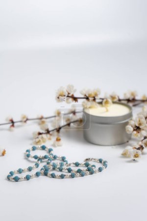 schöne Halskette, eine Kerze und blühende Zweige auf weißem Hintergrund