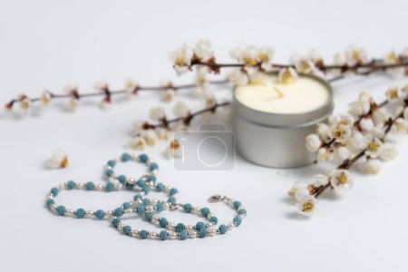 beautiful necklace, a candle and blooming branches on white background