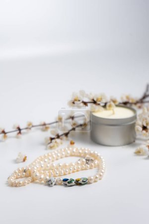Eine Perlenkette, eine Kerze und blühende Zweige auf weißem Hintergrund
