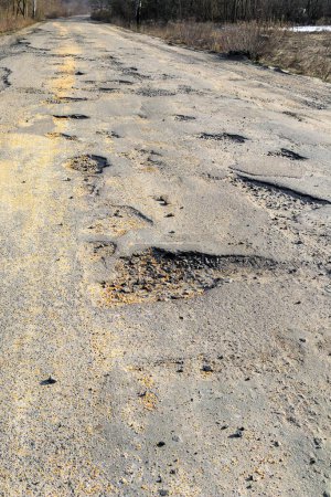 Bad road, cracked asphalt with potholes and large holes. Poor condition of the road, needs repair. Scattered grain on the road