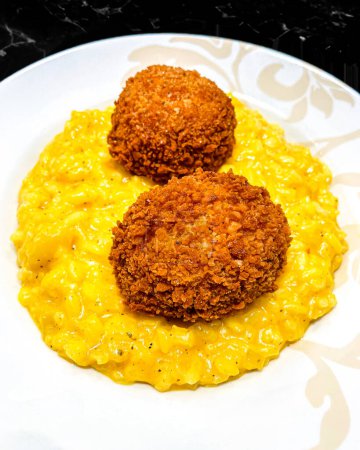 fried croquets with yellow risotto on a white plate