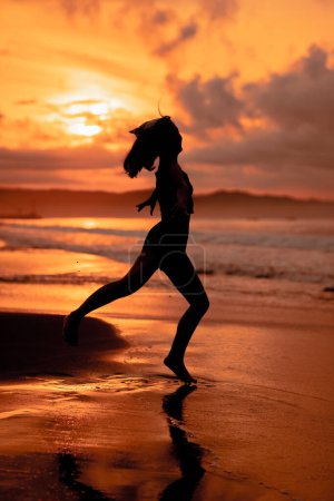 Photo for A ballerina with a silhouette shape performs ballet movements very flexibly on the beach with the waves crashing in the afternoon - Royalty Free Image