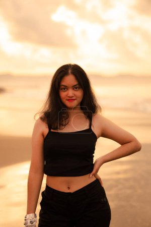 Photo for An Asian teenage girl in a black shirt looks very happy as can be seen from her expression while on vacation by the beach in the afternoon - Royalty Free Image