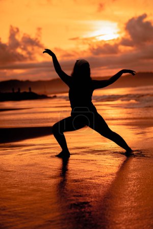 Photo for Silhouette image of an Asian woman doing ballet movements very flexibly on the beach - Royalty Free Image
