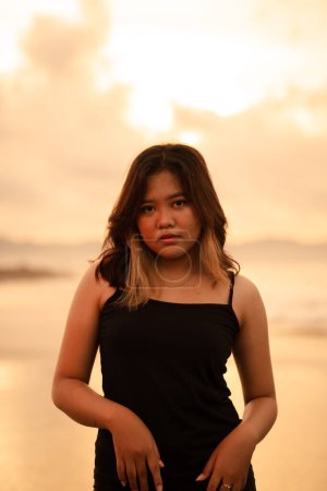 Photo for An Asian woman poses with a dirty and angry expression when wearing a black dress on the beach in the morning - Royalty Free Image