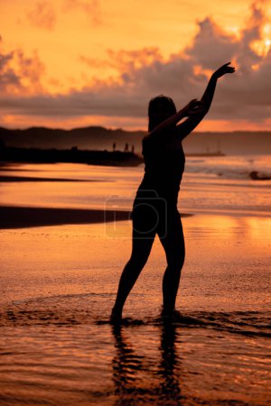 Photo for A Balinese woman in the form of a silhouette performs ballet movements very deftly and flexibly on the beach with the waves crashing in the afternoon - Royalty Free Image