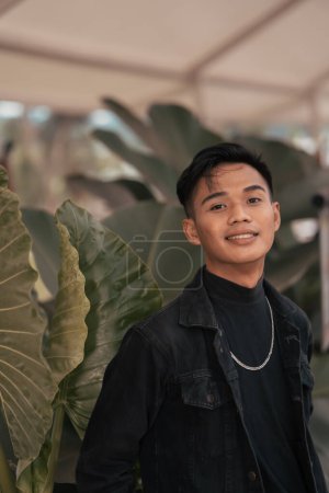 Photo for An asian boy in a black denim jacket posing like a naughty boy with a chain around his neck in a park in the afternoon - Royalty Free Image