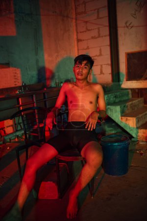 Photo for A man in shorts posing on a chair with colorful lights in an old room - Royalty Free Image