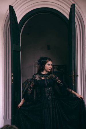 Photo for An Asian woman with lips and a black dress standing in front of an open door while visiting a cemetery in the afternoon - Royalty Free Image