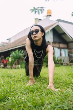 Photo for An Asian woman with sunglasses and a black shirt posing and crawling on the green grass - Royalty Free Image