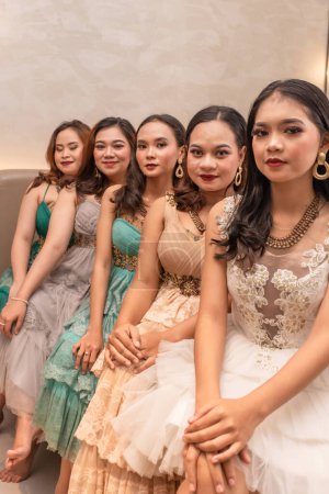 Photo for A group of Asian women sitting together on a white bed while wearing dresses and makeup during a party at a friend's house at night - Royalty Free Image