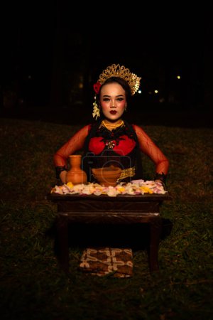 Téléchargez les photos : Plan large d'une fille asiatique en vêtements traditionnels assis dans une forêt avec une table pleine de fleurs la nuit - en image libre de droit