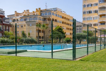 Swimming pool surrounded by grass and large metal fence for safety. Holiday apartments