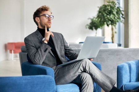 Photo for Pensive businessman working using laptop planning startup  sitting in modern office. Portrait of young confident freelancer sitting at workplace - Royalty Free Image