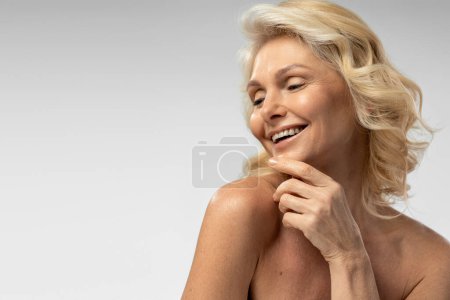 Téléchargez les photos : Attractive 50-55 years old Caucasian blonde mature woman, with fresh healthy glowing skin, smiling a beautiful toothy smile, isolated on white background with copy space. Beauty treatment. Cosmetology - en image libre de droit