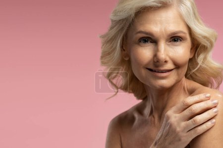 Téléchargez les photos : Close-up portrait of Caucasian 50-55 years old female adult, confident pretty blonde mature woman looking at camera, posing shirtless isolated on pink background. Copy space. Anti-aging beauty concept - en image libre de droit