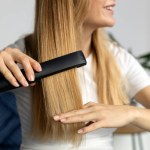 Beautiful smiling woman using hair straightener at home, selective focus on hair. Beauty, hair care concept