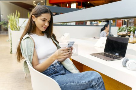 Beautiful smiling woman holding smartphone and shopping online at the mobile app while relaxing at the cafe. Happy attractive female communicating, reading pleasant message. Social media concept 