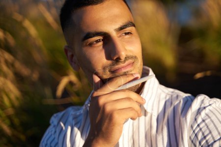 Photo for Closeup portrait of pensive middle eastern man holding pen and looking away, planning something, relaxing in park - Royalty Free Image