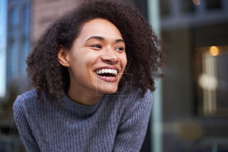 Foto de Retrato de cerca de una mujer joven afroamericana con estilo impresionante que sonríe con una sonrisa alegre, expresando emociones positivas y felicidad. Feliz y exitoso concepto de gente hermosa - Imagen libre de derechos