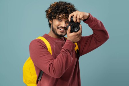 Photo for Smiling Indian photographer holding photo camera taking pictures isolated on blue background. Attractive asian tourist with backpack looking at camera. Travel concept - Royalty Free Image