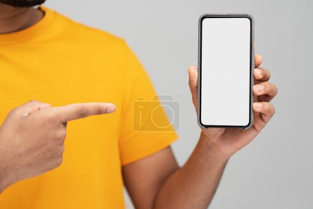Foto de Closeup of man hand holding mobile phone, shopping online pointing finger at empty display isolated on gray background. Mockup. Modern hipster using mobile app, ordering food, selective focus - Imagen libre de derechos