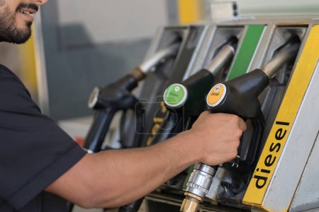 Foto de Cropped view of the man preparing refuelling his car at the gas station. Unknown guy hand holding equipment in filling station in city - Imagen libre de derechos