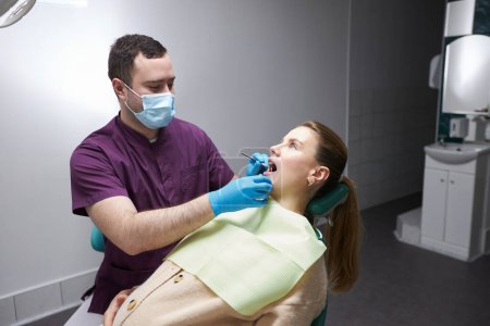 Photo for Caucasian charming young pregnant woman, patient visiting dental hygienist, at regular medical check-up in dentist office. Dentistry. Oral and dental care. Healthcare and medicine concept - Royalty Free Image