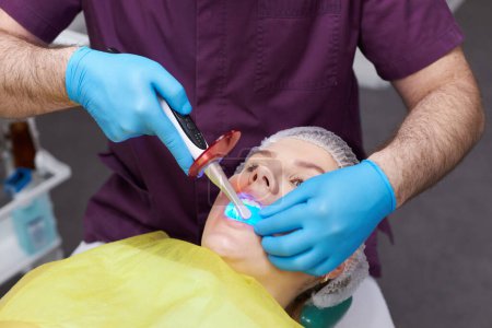 Téléchargez les photos : Gros plan femme enceinte se blanchissant les dents. Blanchiment des dents à la clinique dentaire moderne. Remplissage des dents lampe ultraviolette - en image libre de droit