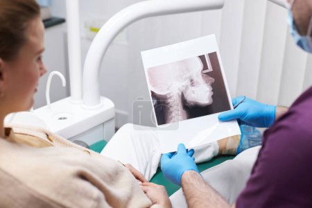 Téléchargez les photos : Close-up dentist orthodontist holding panoramic x-ray film of female teeth, consulting his patient about dental treatment in dentistry clinic. Selective focus on X-Ray orthopantomogram. Dental heath - en image libre de droit