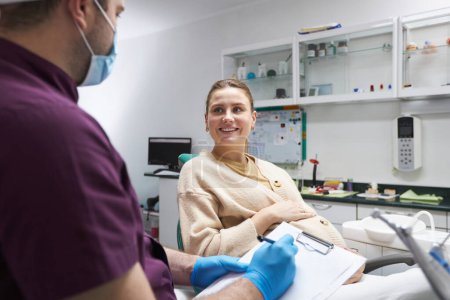 Foto de Young pregnant woman with a beautiful smile listens to the dentist in dental clinic. Orthodontist consulting a pregnant woman, explaining the treatment that needs to do. Dentistry. Oral care - Imagen libre de derechos