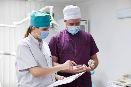 Experienced team of dentists doctors, hygienists , orthodontists consulting each other about the dental treatment of a patient, holding a plastic sample or model of human jaw bone. Stomatology