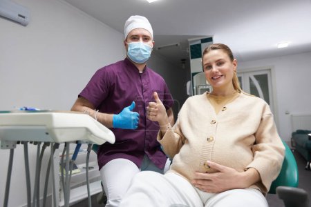 Photo for Dentist doctor and pregnant woman smiling a beautiful toothy smile, gesturing with thumb up at camera after regular dental check-up or teeth treatment in the dental office. People. Service. Healthcare - Royalty Free Image